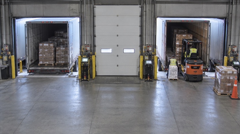 High-angle 3PL dock camera view showing uneven trailer and door activity