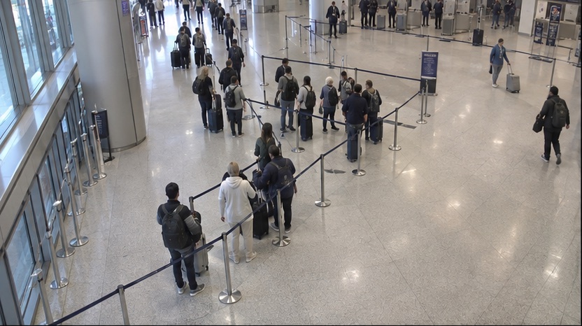 High-angle airport camera view showing a check-in queue beginning to grow