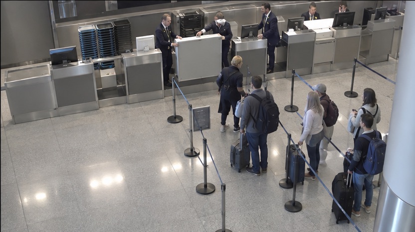 High-angle airport camera view showing staff opening additional service capacity