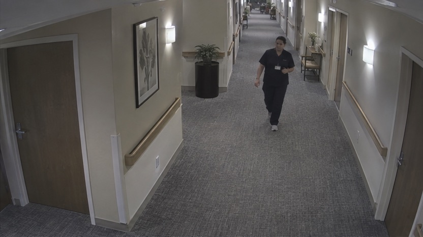High-angle corridor camera view showing a staff member arriving at the monitored area