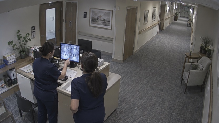 High-angle care facility camera view showing staff reviewing footage during handover