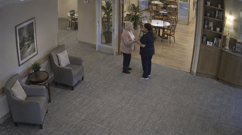 High-angle care facility camera view showing a calm staff follow-up