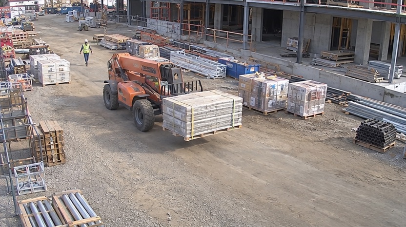 Elevated site camera view showing a telehandler moving palletized material